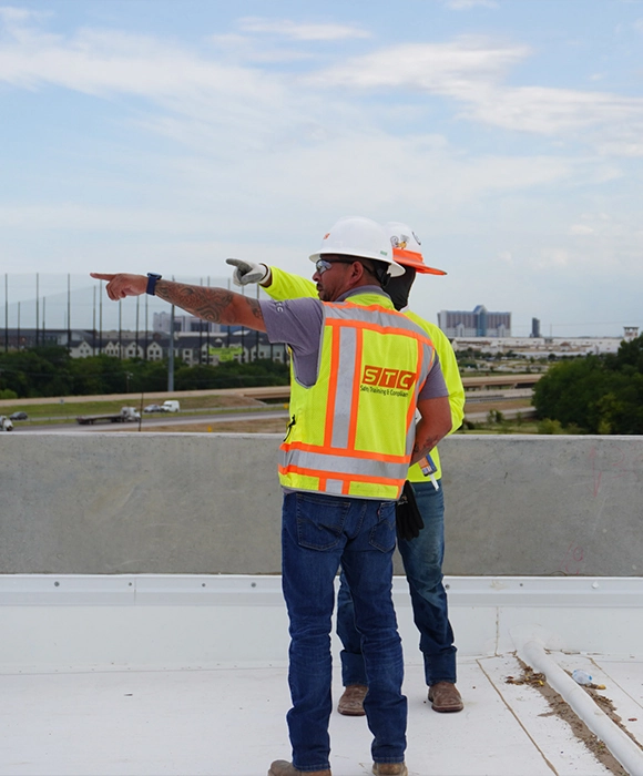 Two men in yellow vests standing side by side and pointing to the left.