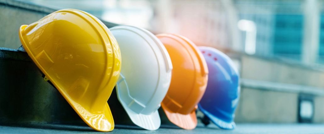 Four hard hats lined up in a row, yellow, white, orange, and blue.